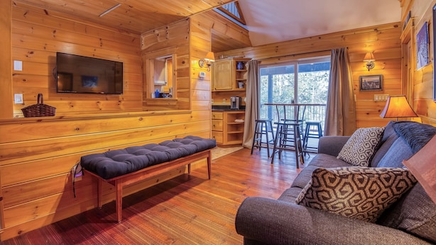 A wooden cabin interior with a sofa, bench, TV, and a balcony with chairs. - 27 Depot - Adorable 2 bedroom, 2 bath cottage close to the village (Rangeley)