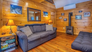 A cozy cabin interior with a sofa, a lamp, a fireplace, and framed pictures on the walls. - 27 Depot - Adorable 2 bedroom, 2 bath cottage close to the village (Rangeley)
