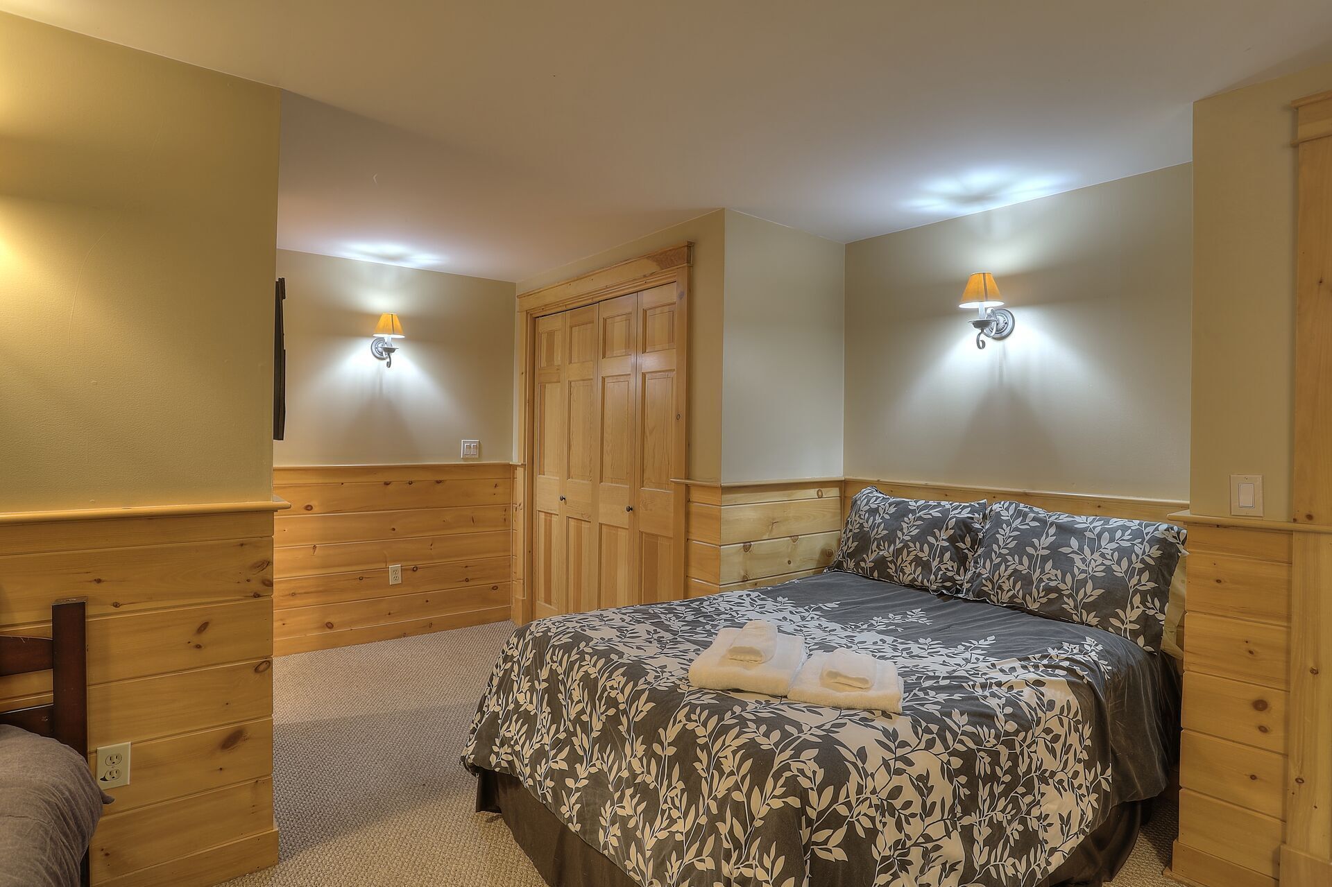 A bedroom with a bed, wooden wardrobe, and two wall-mounted lamps.