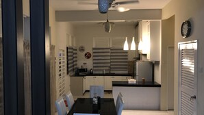 A modern kitchen with white cabinets, a black countertop, and a dining area with a black table and white chairs. - Cozy Scandinavian Bungalow near KLIA & Sepang F1 (KOTA SERIEMAS)