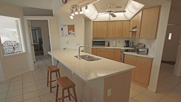A kitchen with a large island, wooden cabinets, a microwave, and a ceiling fan.