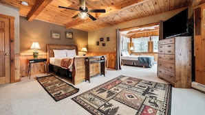 Een slaapkamer in een houten hut met een bed, bedlampjes, een dressoir en een plafondventilator.
