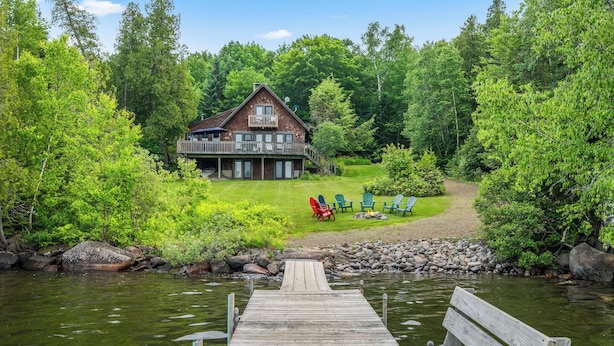 Eine Holzsteg, der zu einem Haus mit Terrasse führt, umgeben von üppigem Grün und einem Fluss.