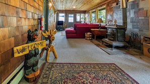 Ein Holzblockhaus-Interieur mit einem roten Sofa, einem Kamin, einem Willkommen-Schild und einer Bärenstatue.