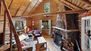A log cabin interior with a stone fireplace, wooden furniture, and a cozy seating area. - Rock Ledge - Relax & Renew in turn-of-century log cabin with side cabin (Rangeley)