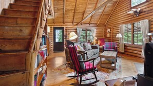 A log cabin interior with a staircase, a rocking chair, a sofa, and a television. - Rock Ledge - Relax & Renew in turn-of-century log cabin with side cabin (Rangeley)