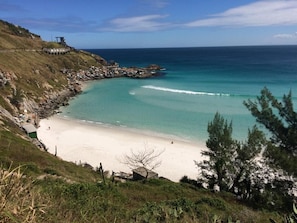 A coastal beach with a sandy shore, a rocky outcrop, and a few buildings.
