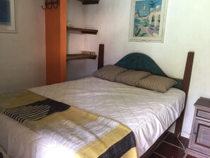 Un letto con una coperta trapuntata e cuscini, una testiera in legno, uno scaffale e un quadro appeso al muro.