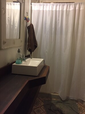 Un bagno con un lavandino bianco, uno specchio, un asciugamano appeso al muro e una tenda da doccia.