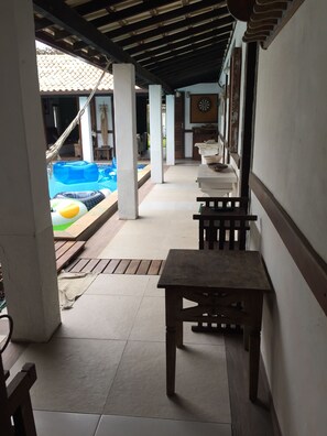 Un'area esterna coperta con piscina, panche in legno e pavimento piastrellato.