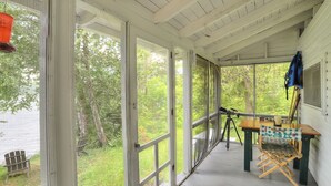 A covered porch with a table and chairs, a telescope, and a chair with a blanket. - Greenvale Cove 8 - Greenvale Cove cottage community on Rangeley Lake (Rangeley)