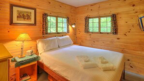 A wooden-paneled room with a bed, two windows with curtains, a lamp, and a framed picture on the wall. - Greenvale Cove 8 - Greenvale Cove cottage community on Rangeley Lake (Rangeley)