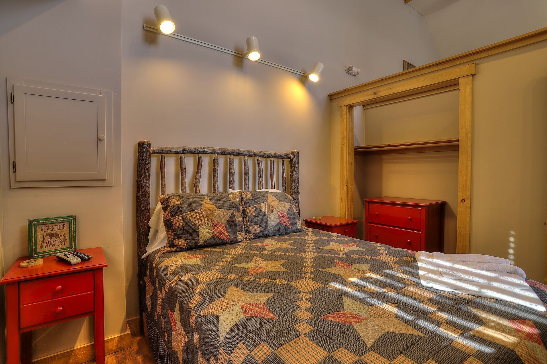 Una camera da letto con una testiera in legno, una coperta trapuntata, un comodino rosso con un telecomando e un comò rosso.