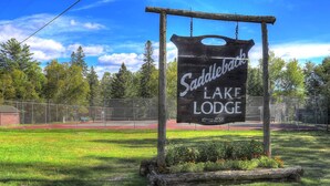 Opastekyltti, jossa lukee ”Saddlebock Lake Lodge”, ja jossa on maalaishenkinen puukehys sekä siitä roikkuva ketju.