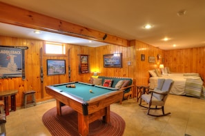 Een pooltafel in een kamer met houten lambrisering, een bank en een bed.