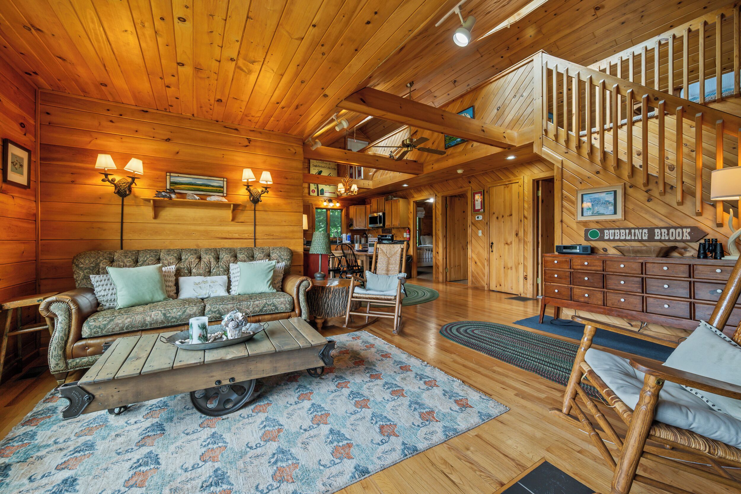 Interior acogedor de una cabaña de madera con sala de estar, comedor y una escalera que lleva a un nivel superior.
