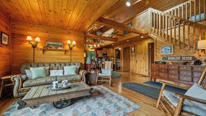 A cozy log cabin interior with a living room, dining area, and a staircase leading to an upper level. - Saddleback Lake Lodge 33 | Close to Saddleback (Rangeley)