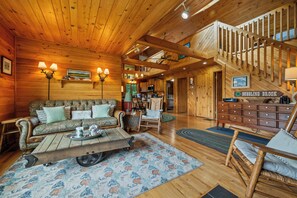 Accogliente interno di una baita in legno con soggiorno, zona pranzo e una scala che conduce a un piano superiore.