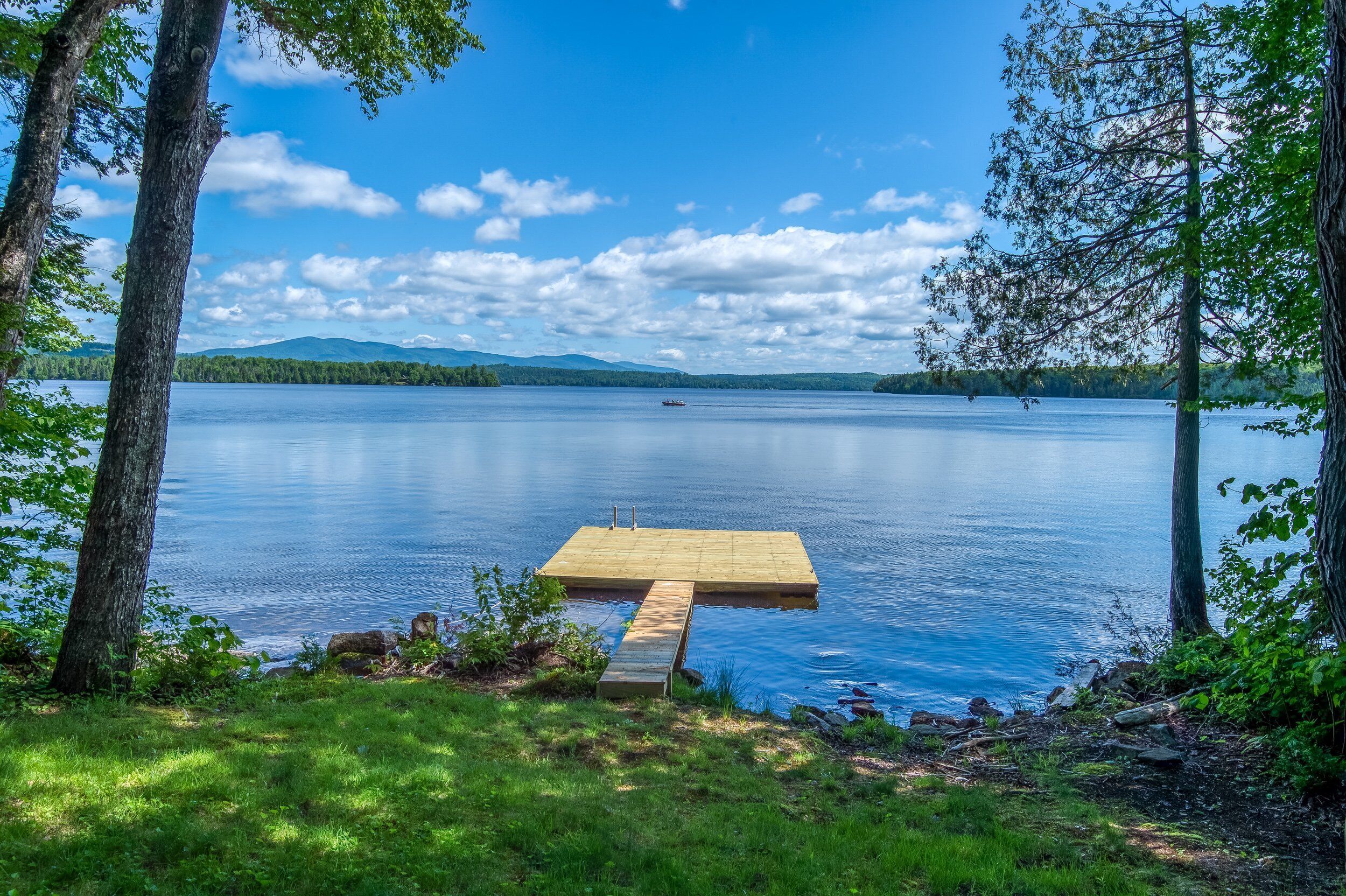 Une jetée en bois s’étendant sur un lac paisible, entouré d’arbres.