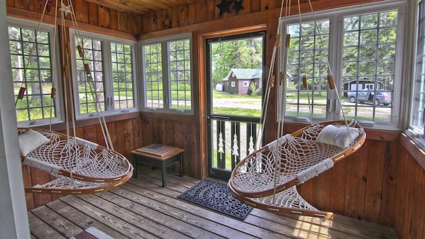 A wooden cabin with two hanging hammocks, a bench, and large windows offering views of the outdoors. - Rangeley Manor A | Nice Cottage Close to Shared Waterfront on Rangeley Lake (Rangeley)
