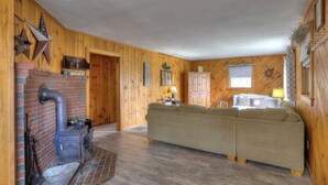 A cozy room with a fireplace, wooden walls, a sofa, and a bed. - Rangeley Manor A | Nice Cottage Close to Shared Waterfront on Rangeley Lake (Rangeley)