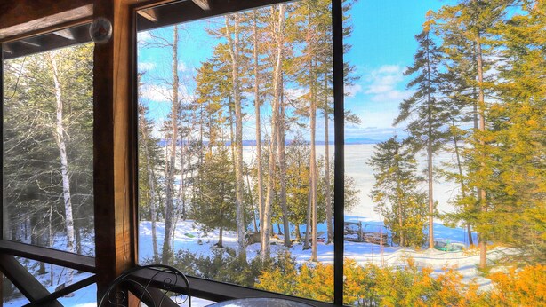 Eine Hütte mit einem großen Fenster mit Blick auf einen verschneiten Wald und einen See.
