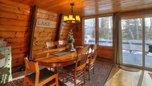 Interior d'una cabana de fusta amb una taula de dinar, cadires, un penjó i un arbre de Nadal, juntament amb un rètol que diu "LAKE".