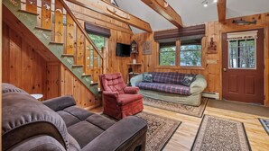 Un intérieur en bois avec un escalier, un fauteuil rouge, un canapé et un téléviseur.