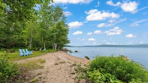 Une plage avec un sentier de sable menant à une zone herbeuse où se trouvent des chaises Adirondack bleues.