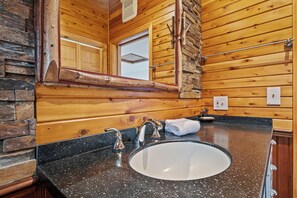 Une salle de bain avec un lavabo à vasque en granit, des murs en bois, un grand miroir et une serviette accrochée au mur.