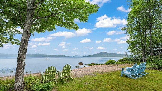 Une vue sur le lac, avec une pelouse, deux fauteuils Adirondack verts et une table.