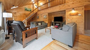 Ein Holzinnenraum mit Treppe, grauem Sofa, Ledersessel und Flachbildfernseher.