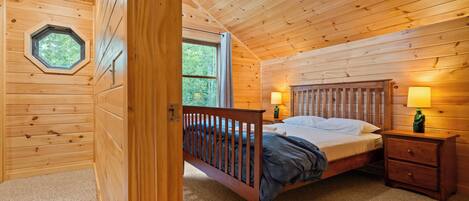 A wooden cabin bedroom with a bed, nightstands, and a window.