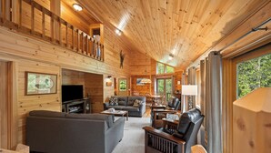 Ein geräumiges Holzblockhaus-Interieur mit Wohnbereich, einer Couch, einem Fernseher und einem Essbereich.