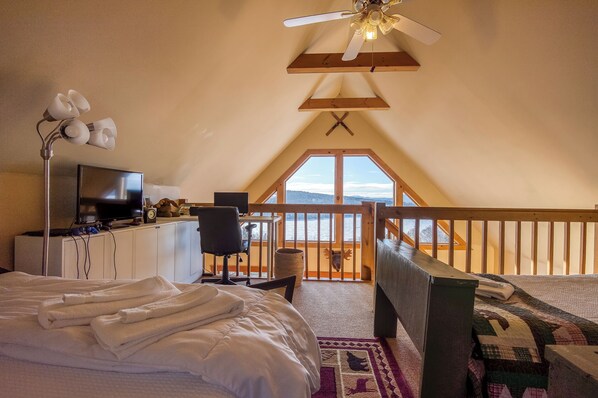 A bedroom with a bed, a desk, a TV, and a view of the outdoors.