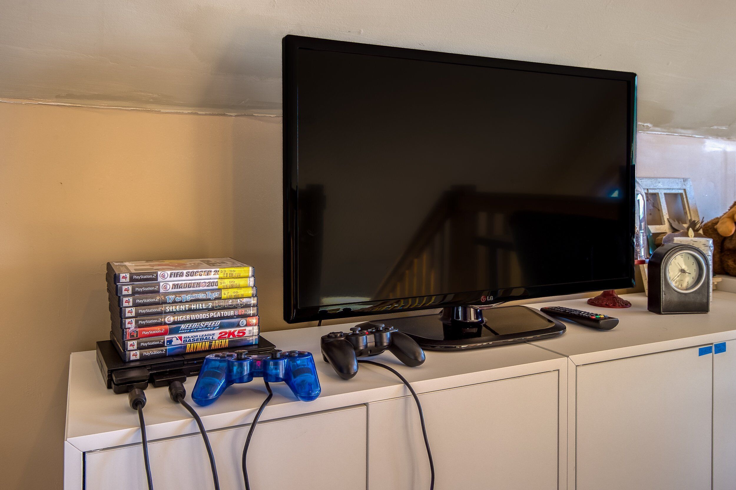 A television, video games, and a clock on a white cabinet.