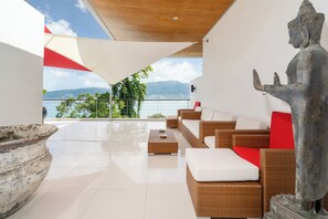 A modern outdoor lounge area with wicker furniture, a large stone sculpture, and a view of mountains and water. - Villa 5 Oceanfront pool villa (Patong)