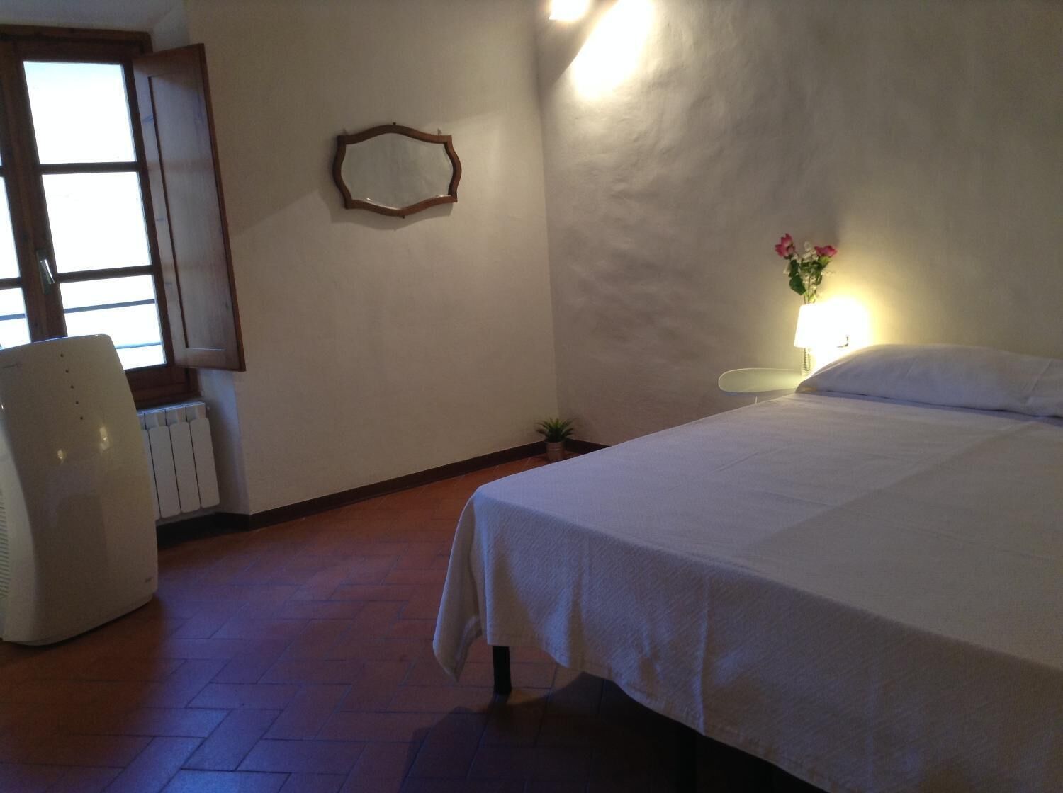 A bedroom with a bed, a chair, a radiator, a mirror, and a window.