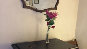 Un mueble de madera oscura con una computadora portátil encima, un florero con flores y un espejo con fotografías en la pared.