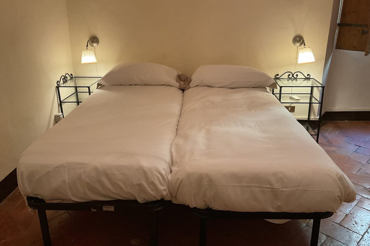 Una cama doble con ropa de cama blanca, dos mesitas de noche con lámparas y un suelo de baldosas.