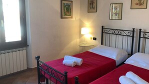 Habitación de hotel con dos camas individuales, una mesita de noche con lámpara y una ventana con persianas.