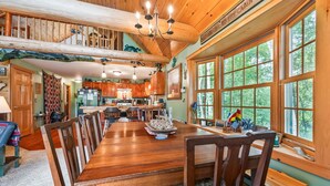 Un comedor amplio con una gran mesa y sillas de madera, una araña y ventanas grandes con vistas al exterior.