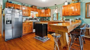 A kitchen with wooden cabinets, a stainless steel refrigerator, a stove, and a microwave. - Alpine Loon Lodge - Just a mile from downtown Rangeley with lake views! (Rangeley)