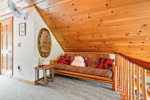 A cozy room with a wooden ceiling, a sofa with patterned cushions, a small table, and a mirror.