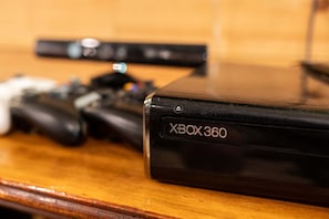 Uma superfície de madeira com um console Xbox 360 e um controle preto.