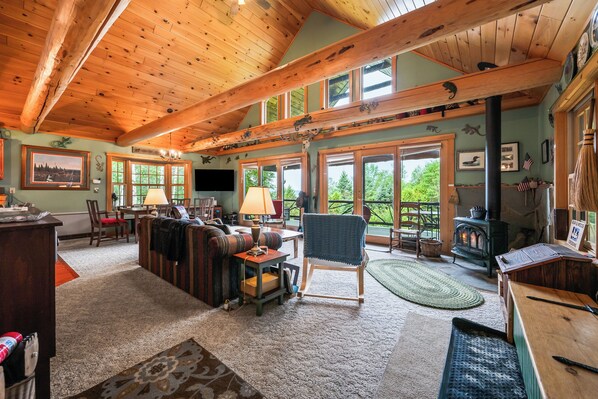 A spacious living room with a high wooden ceiling, large windows, and a cozy fireplace.