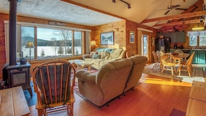 L’intérieur chaleureux d’un chalet, avec une cheminée, des meubles en bois et de grandes fenêtres donnant sur le paysage enneigé.