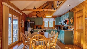 L’intérieur d’un chalet en bois comprend une table à manger et des chaises, une cuisine avec des meubles verts et une grande fenêtre.
