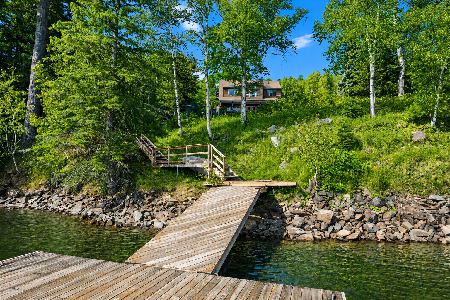 A wooden dock leading to a house surrounded by greenery and trees.