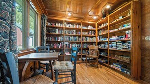 Une bibliothèque chaleureuse avec des étagères en bois, une table à manger et des fauteuils confortables.